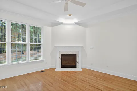 a view of an empty room with wooden floor fireplace and a window