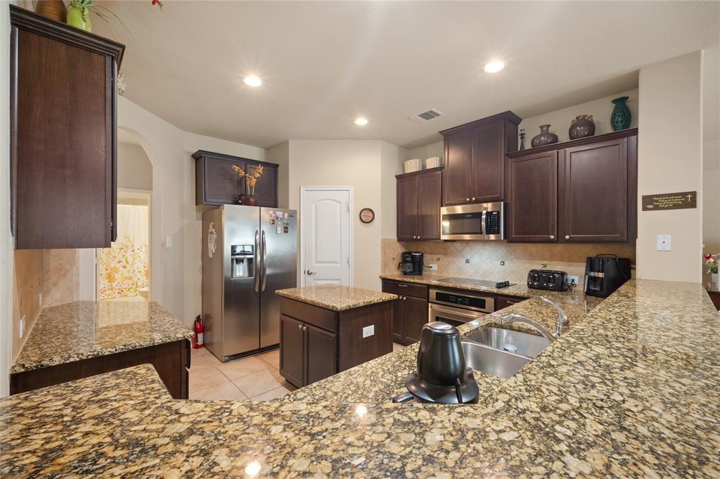 520 Rustic Oak Lane McKinney, TX 75072 - Photo 10 of 30 Spacious kitchen featuring extensive granite countertops, dark wood cabinetry, stainless steel appliances, a center island, and recessed lighting