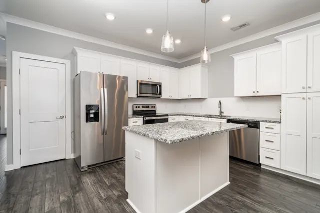 a kitchen with stainless steel appliances granite countertop a refrigerator a stove a sink and white cabinets with wooden floor