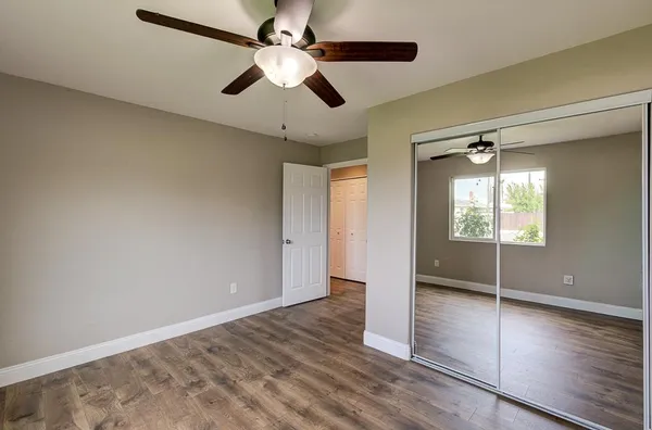 an empty room with wooden floor fan and windows