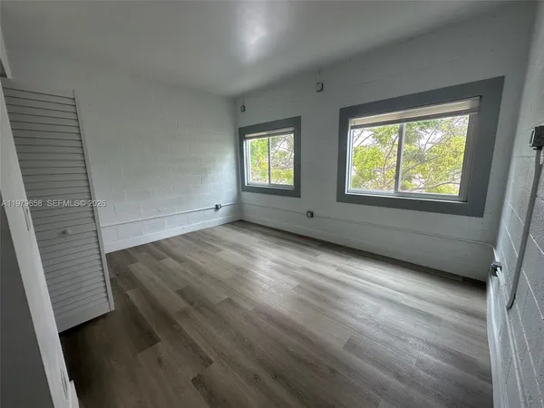 a view of an empty room with wooden floor and a window