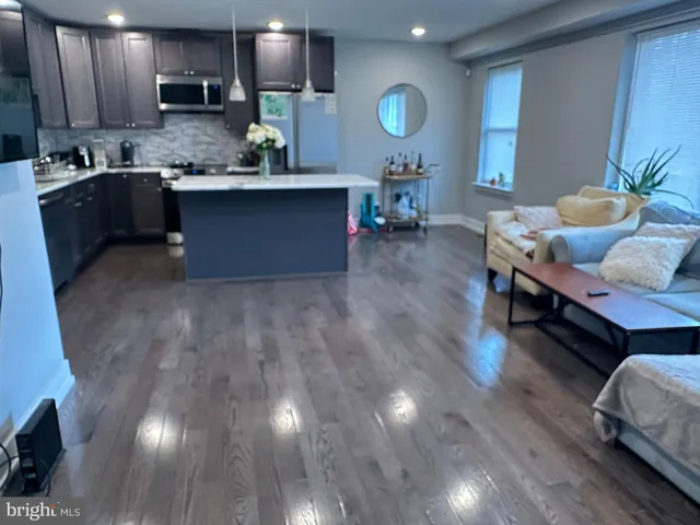 a living room with stainless steel appliances granite countertop furniture a wooden floor and a sink