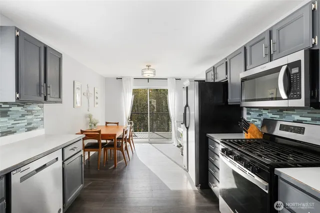 a kitchen with stainless steel appliances a stove a sink dishwasher a refrigerator with a dining table and chairs