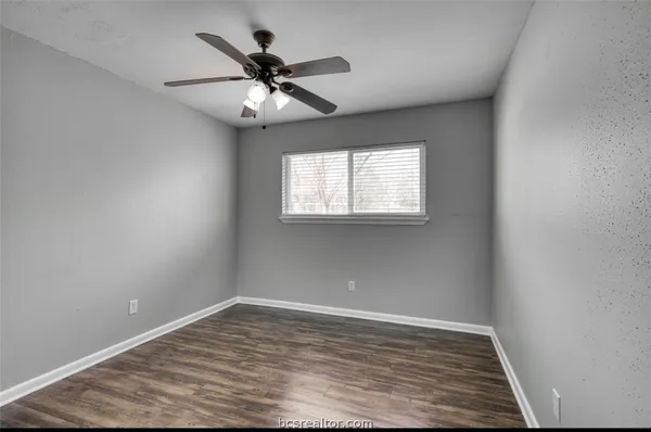 an empty room with wooden floor fan and windows