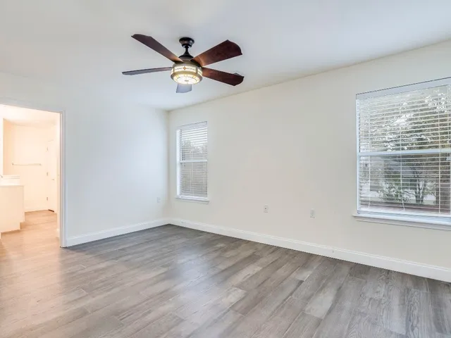 an empty room with wooden floor fan and windows