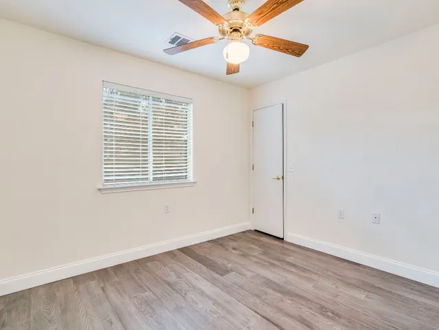 an empty room with wooden floor chandelier fan and windows