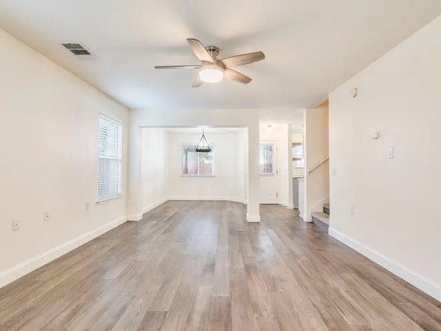 a view of an empty room with wooden floor and a ceiling fan