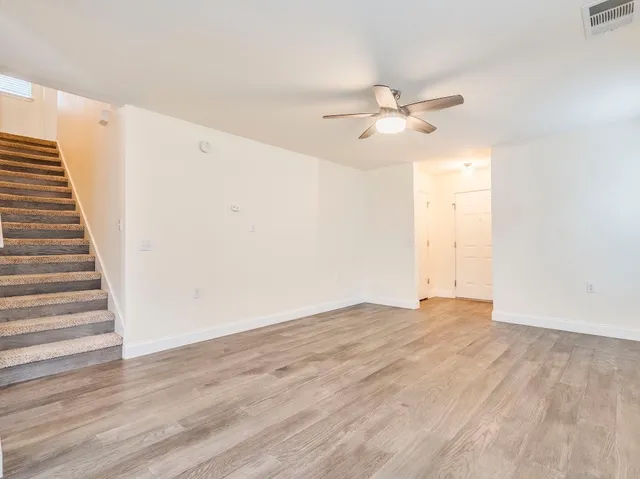 a view of an empty room with wooden floor and a ceiling fan