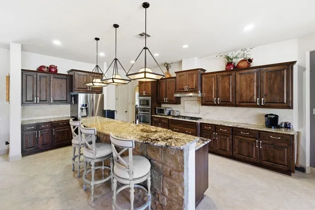 a kitchen with stainless steel appliances kitchen island granite countertop a table chairs and a refrigerator