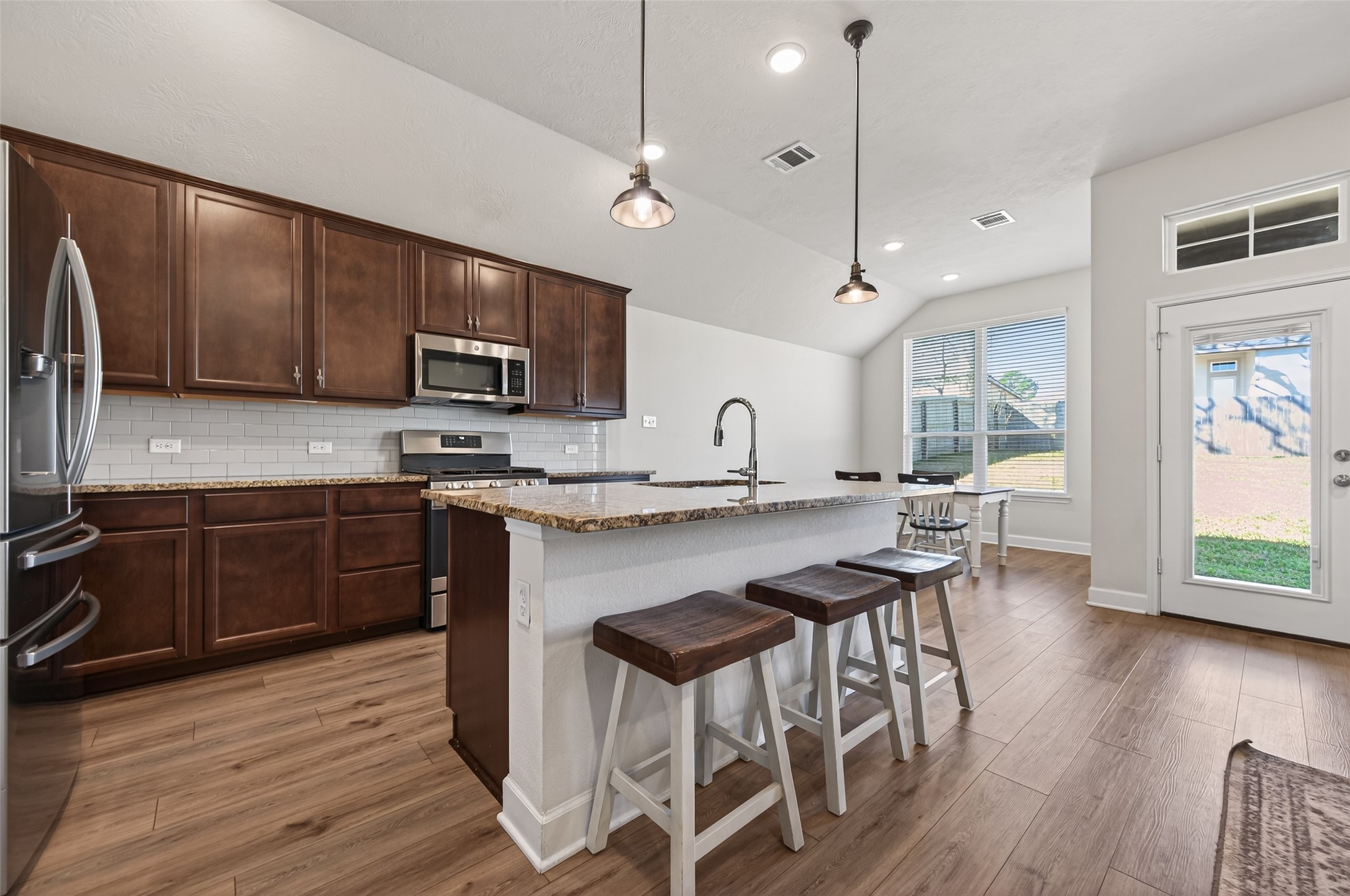917 Farm Path Brenham, TX 77833 - Photo 12 of 43 a kitchen with stainless steel appliances kitchen island granite countertop a stove a refrigerator a sink a dining table and chairs with wooden floor