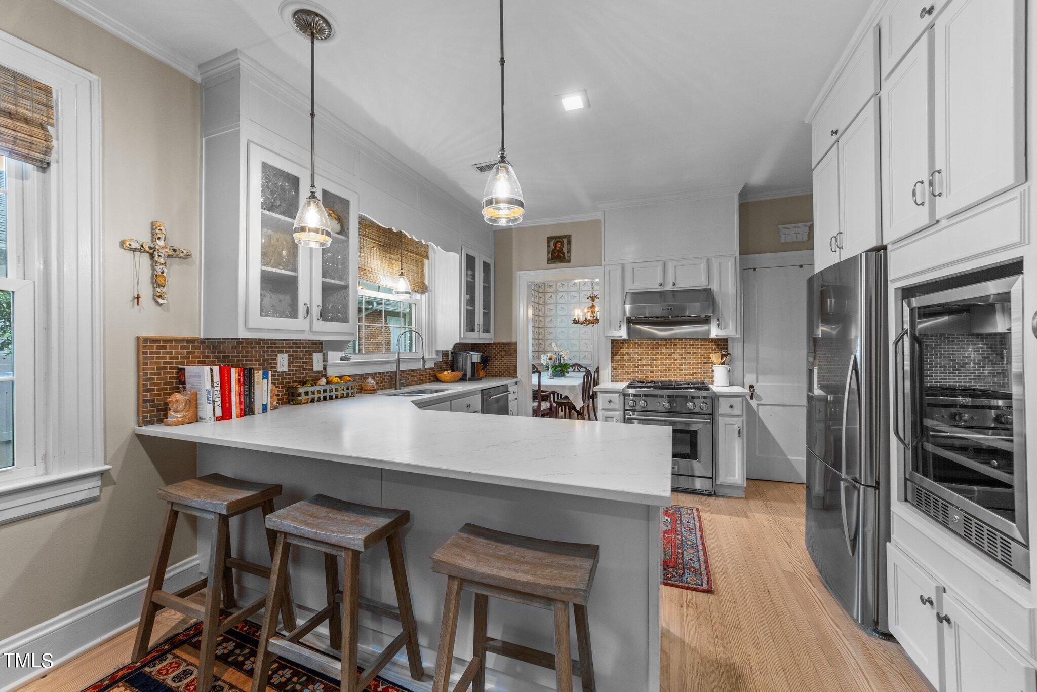 2219 Creston Road Raleigh, NC 27608 - Photo 16 of 45 a kitchen with stainless steel appliances granite countertop a stove a refrigerator a kitchen island a sink dishwasher a dining table and chairs with wooden floor