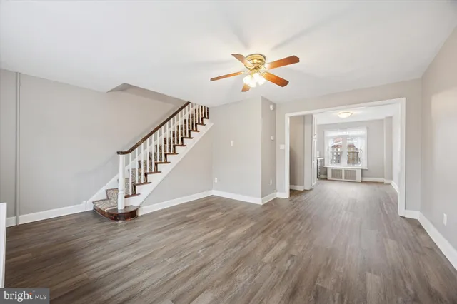 a view of an empty room with wooden floor and a ceiling fan
