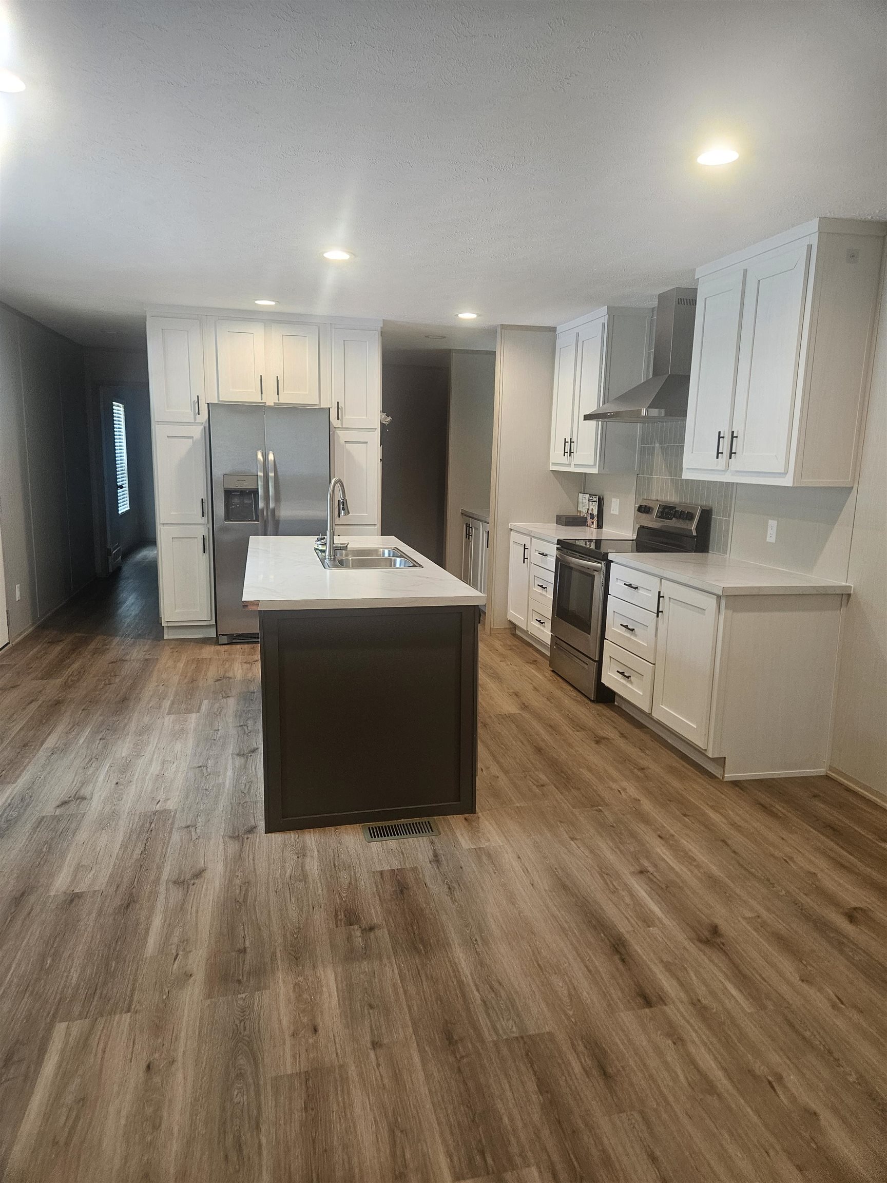 75 Pittman Road, Unit ROAD Somerville, TN 38068 - Photo 11 of 26 Modern kitchen featuring wood-finish flooring, white cabinetry, a dark-toned island with a stainless steel sink, stainless steel appliances, and recessed lighting