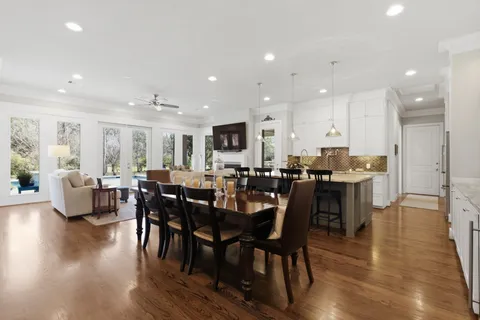 a view of a dining room and livingroom with furniture wooden floor a rug a fireplace and a kitchen
