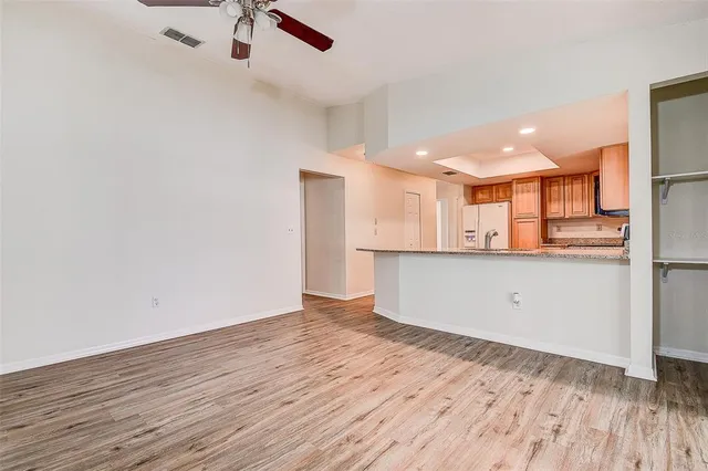 an empty room with wooden floor kitchen view and windows