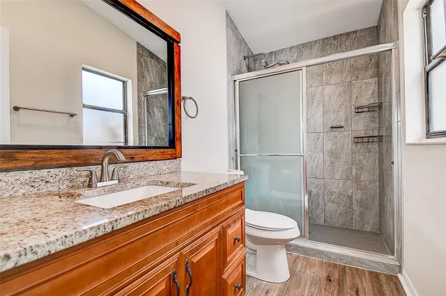 a bathroom with a granite countertop shower sink vanity mirror and toilet