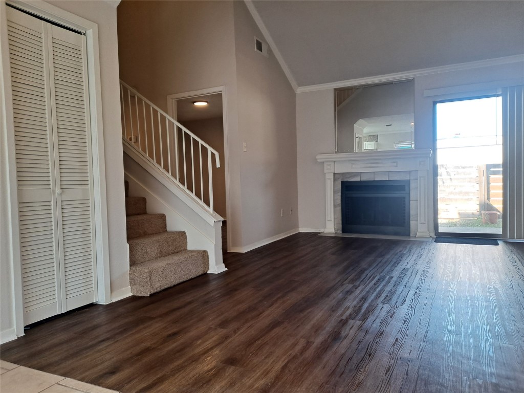Unfurnished living room featuring stairs, dark wood-style floors, a tile fireplace, vaulted ceiling, and ornamental molding