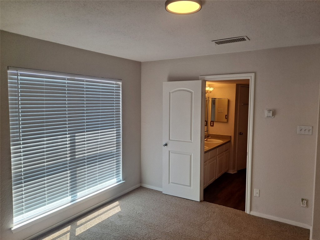 2018 West Rundberg Lane, Unit 9B Austin, TX 78758 - Photo 15 of 23 Unfurnished bedroom featuring dark carpet, a textured ceiling, and connected bathroom