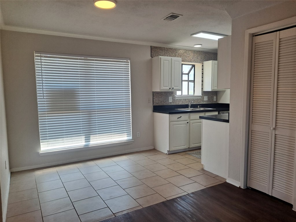 2018 West Rundberg Lane, Unit 9B Austin, TX 78758 - Photo 7 of 23 Kitchen with light tile patterned flooring, dark countertops, white cabinets, backsplash, and crown molding