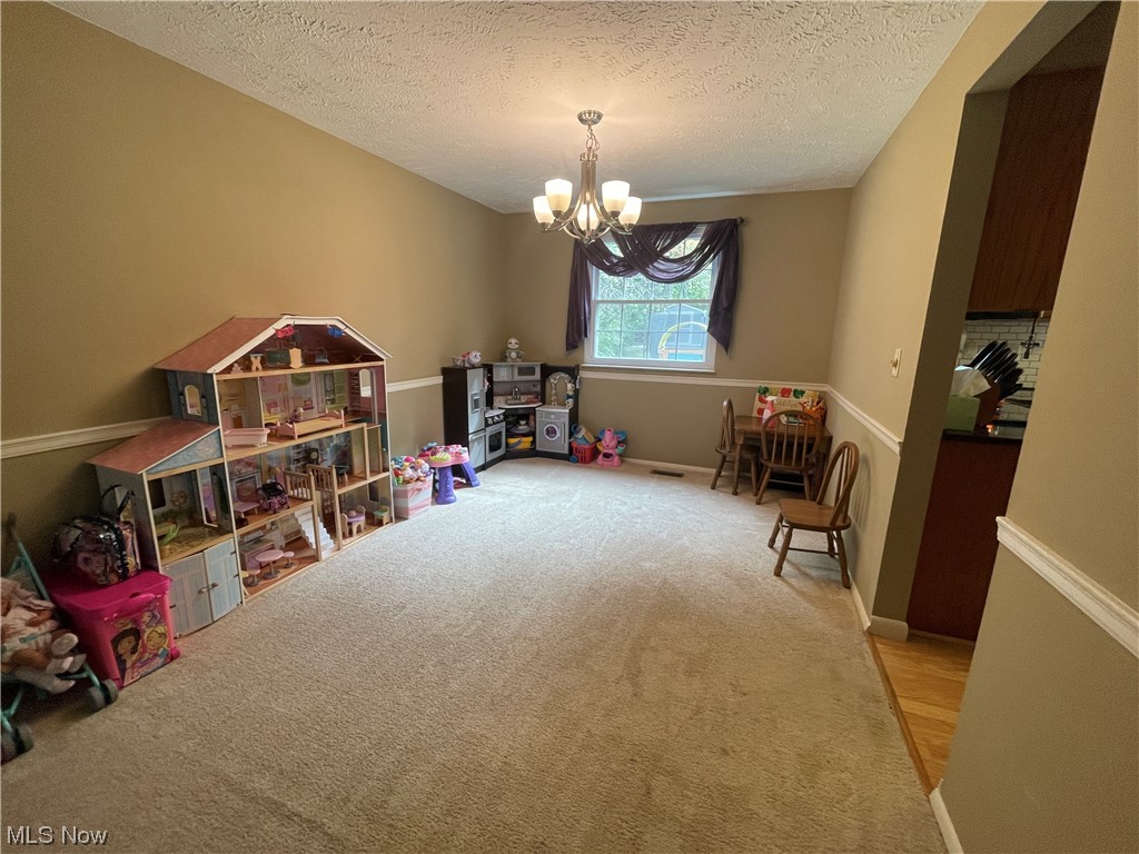 Carpeted dining room with chandelier, currently used as playroom.