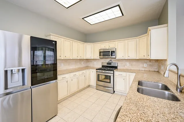 a kitchen with stainless steel appliances kitchen island granite countertop a dining table chairs and a refrigerator