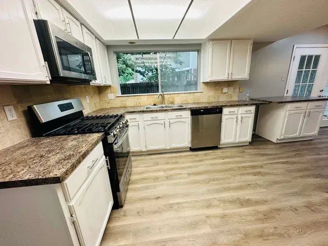 a kitchen with stainless steel appliances granite countertop a stove a sink dishwasher and a microwave oven with white cabinets