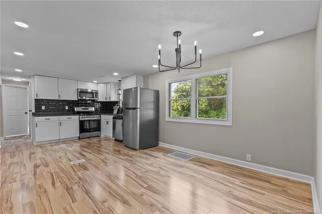 a kitchen with stainless steel appliances granite countertop a refrigerator a sink dishwasher a stove and white cabinets with wooden floor