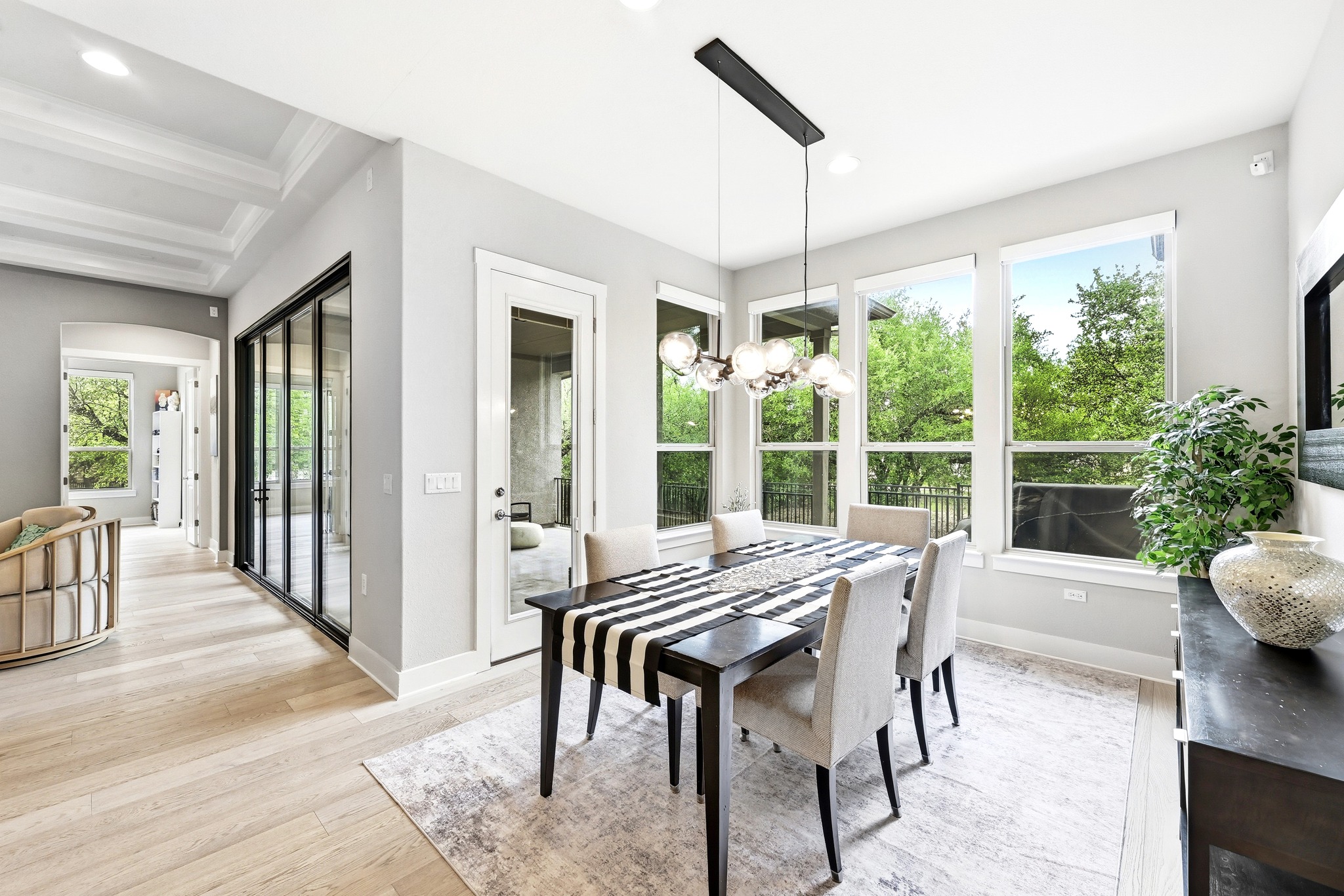 9008 Harper Rae Drive Austin, TX 78717 - Photo 10 of 39 Dining area with expansive windows, light wood-finish flooring, a contemporary chandelier, a glass-paneled exterior door, and a coffered ceiling in the adjacent hallway