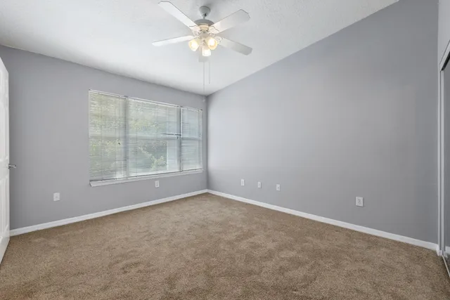 an empty room with chandelier fan and windows