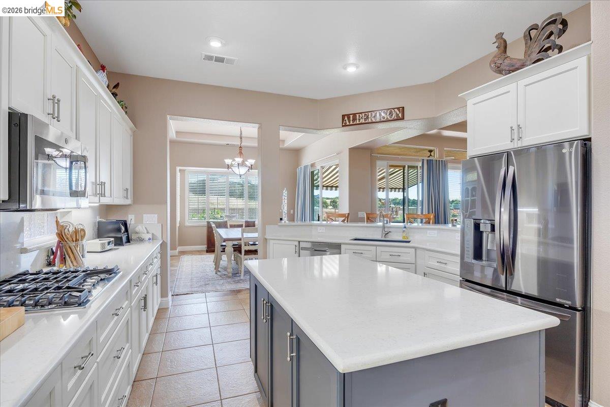 158 Rock Ridge Lane Copperopolis, CA 95228 - Photo 25 of 72 Open-concept kitchen featuring an island with a light-toned countertop, stainless steel appliances, white cabinetry, a built-in microwave, and tile flooring