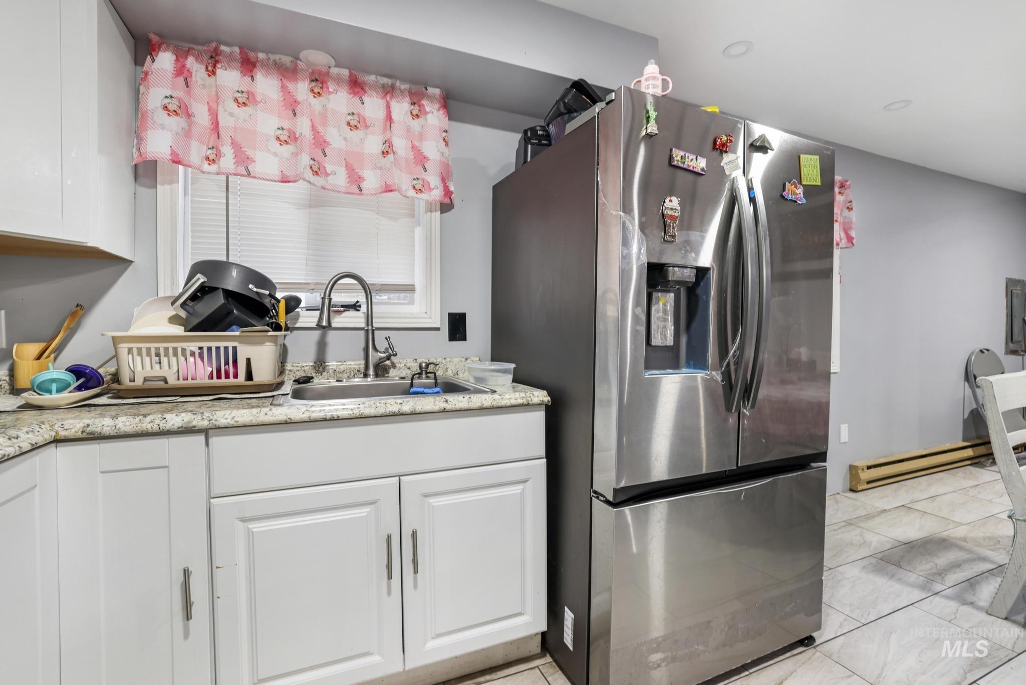 403 3rd Avenue West Jerome, ID 83338 - Photo 19 of 36 Kitchen featuring stainless steel refrigerator with ice dispenser, white cabinetry, and a baseboard heating unit