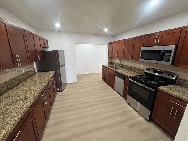 a large kitchen with stainless steel appliances granite countertop a stove top oven a sink dishwasher a refrigerator and a microwave oven