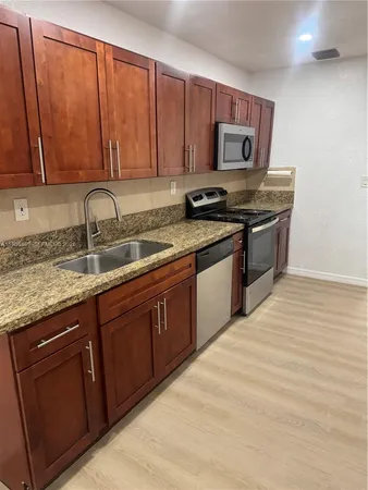 a kitchen with stainless steel appliances granite countertop a stove a sink dishwasher and a microwave oven with wooden cabinets