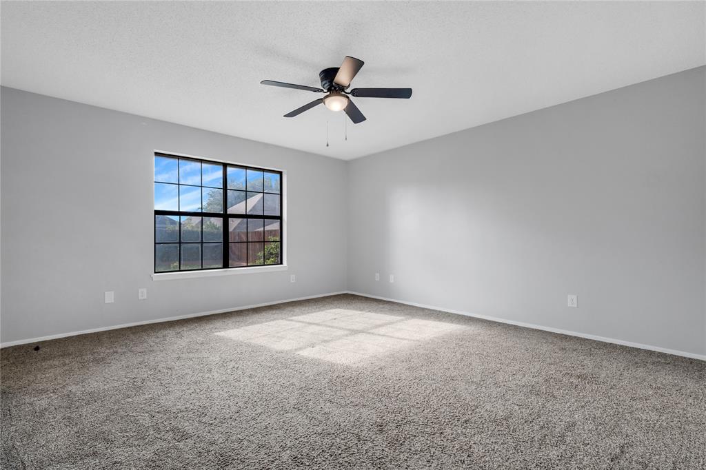 1609 Robin Street Mineola, TX 75773 - Photo 17 of 24 Spacious room featuring neutral carpeting, light gray wall tones, a large window with black gridding, and a ceiling fan with integrated lighting