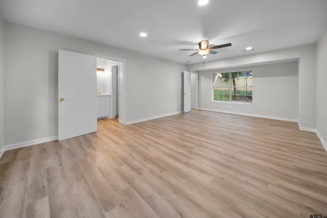 an empty room with wooden floor ceiling fan and windows
