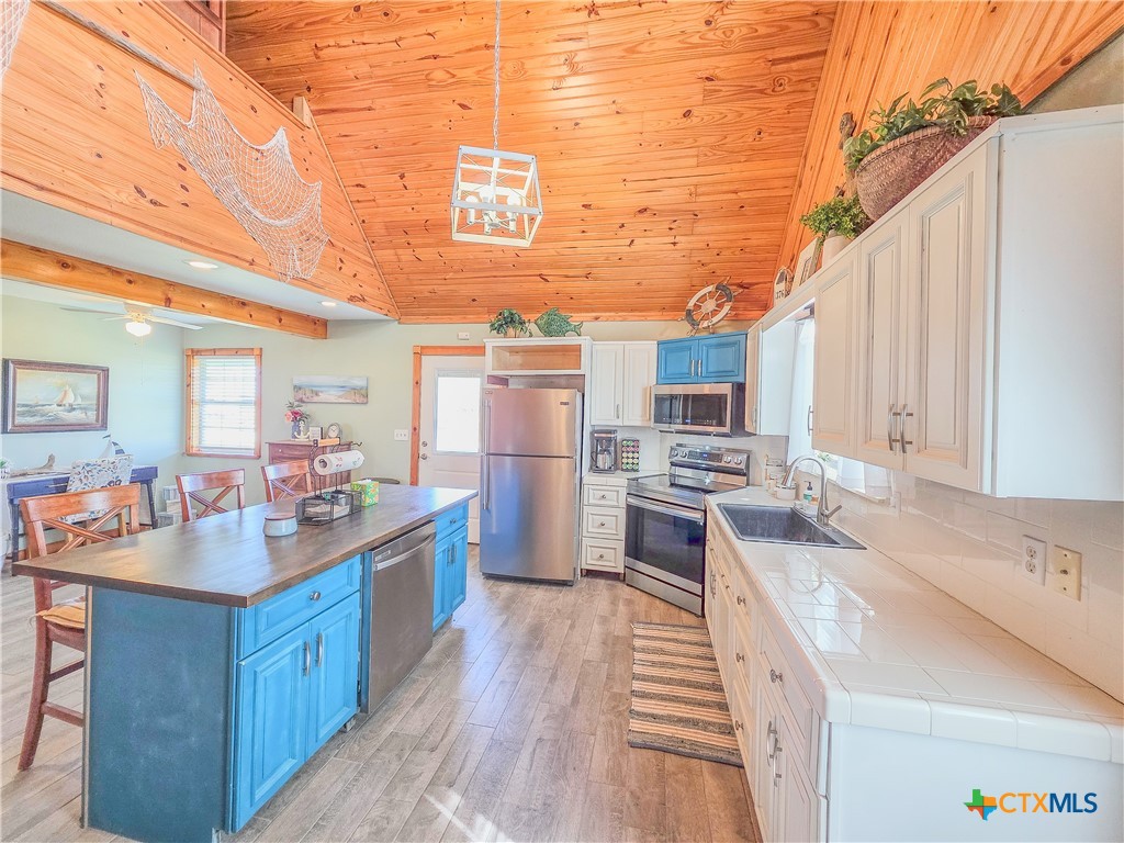 376 Haddock Drive Palacios, TX 77465 - Photo 41 of 41 This spacious kitchen features high wooden ceilings and a cozy open floor plan. It includes modern stainless steel appliances, a central island with vibrant blue cabinetry, and ample counter space. Natural light enhances its warm, inviting atmosphere, making it perfect for family gatherings.