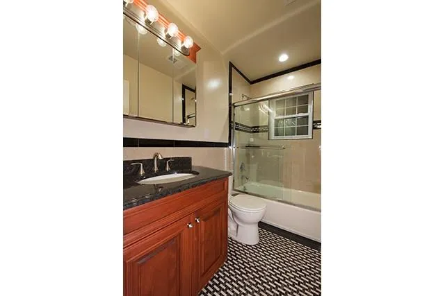 a bathroom with a granite countertop sink a toilet a mirror and shower