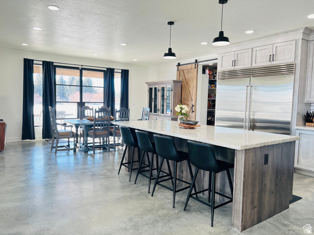 100 Whit Lane Georgetown, ID 83239 - Photo 6 of 76 Two tone kitchen featuring finished concrete flooring, stainless steel built in fridge, a barn door, a kitchen island, and light stone counters