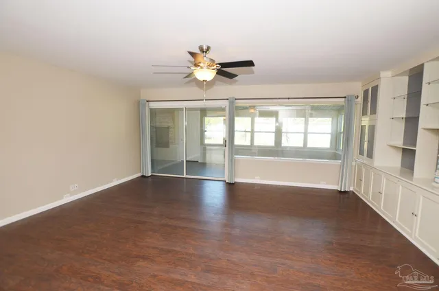 an empty room with wooden floor ceiling fan and window