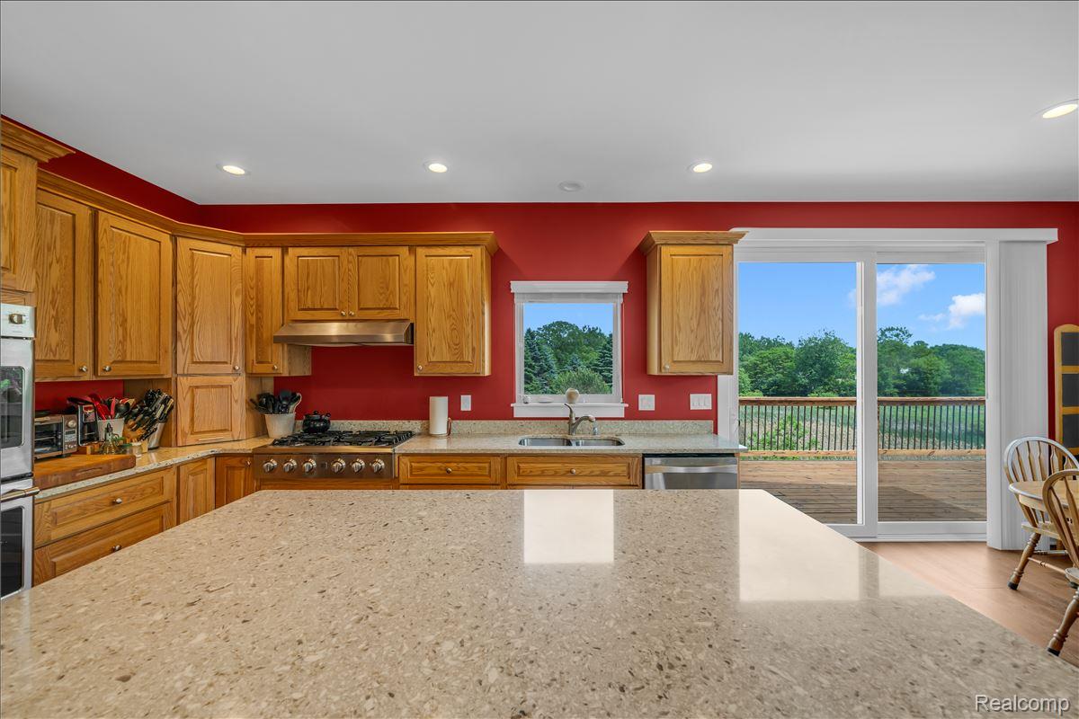 4266 McCandlish Road Grand Blanc, MI 48439 - Photo 22 of 68 Kitchen featuring a large central island with a light-toned countertop, wood-finish cabinetry, built-in double oven, and stainless steel appliances