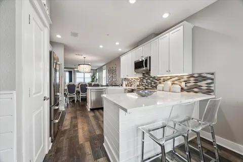 a kitchen with stainless steel appliances kitchen island granite countertop a stove a refrigerator a sink a oven and white cabinets with wooden floor