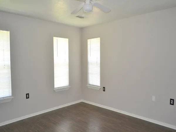 an empty room with wooden floor windows and fan