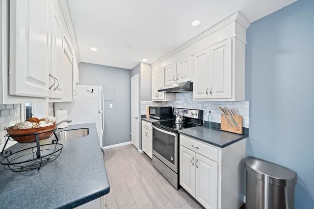 a kitchen with stainless steel appliances granite countertop a stove a sink dishwasher and a refrigerator with white cabinets