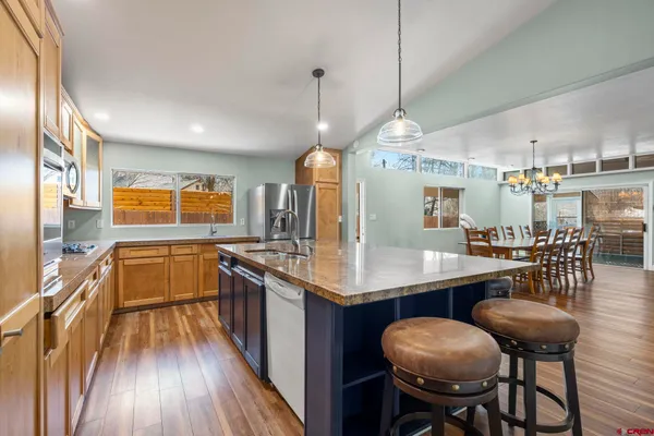 a kitchen with stainless steel appliances granite countertop a stove top oven a sink dishwasher a dining table and chairs with wooden floor