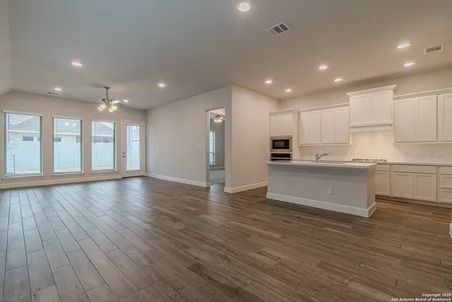 a view of kitchen with granite countertop refrigerator oven and white cabinets with wooden floor