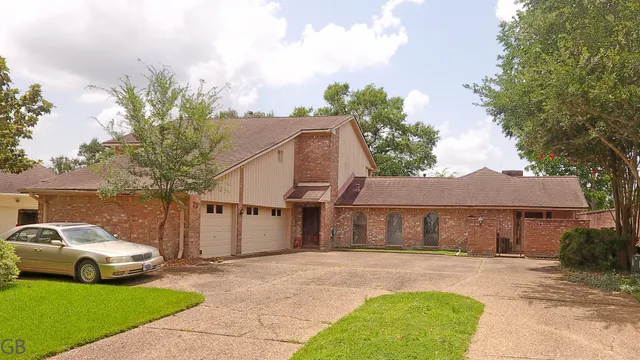 a view of a white house with a yard plants and large tree