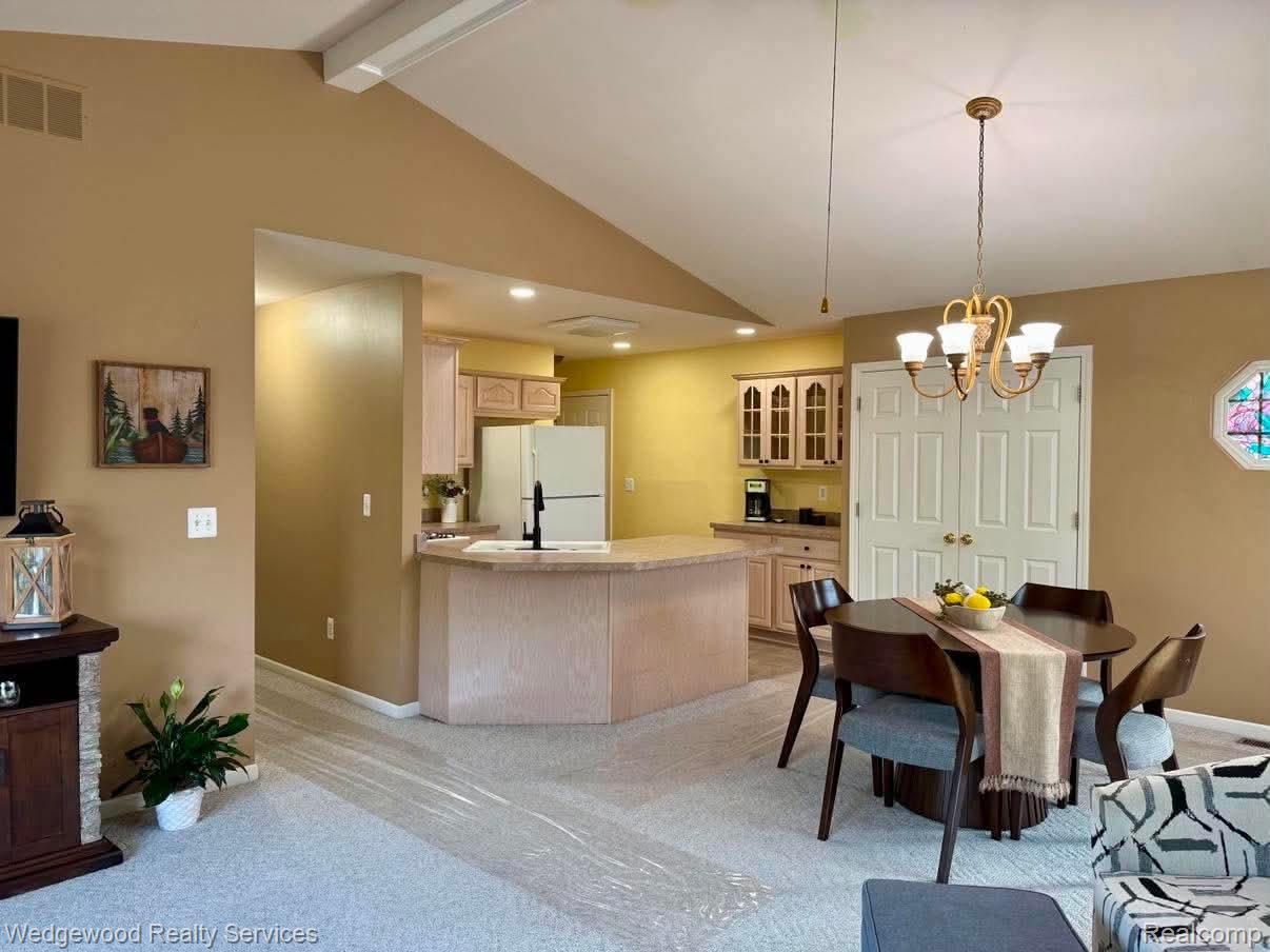 492 Harvard Drive, Unit 84 Romeo, MI 48065 - Photo 9 of 30 Vaulted ceiling with exposed beam, kitchen with built-in cabinetry, breakfast bar, and a dining area with a chandelier