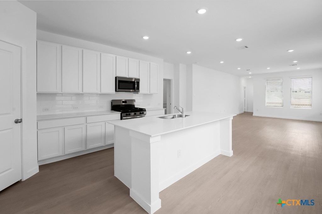 247 Flathead New Braunfels, TX 78130 - Photo 7 of 17 Kitchen with dark wood-style floors, stainless steel appliances, white cabinetry, a kitchen island with sink, and recessed lighting