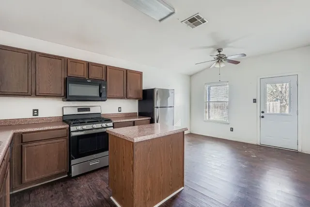 a kitchen with stainless steel appliances granite countertop a stove top oven a sink dishwasher and a refrigerator with wooden floor