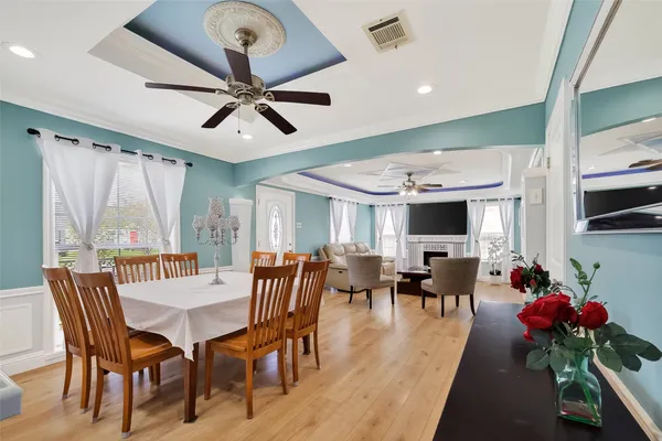 a dining room with wooden floor a chandelier fan a wooden table and chairs